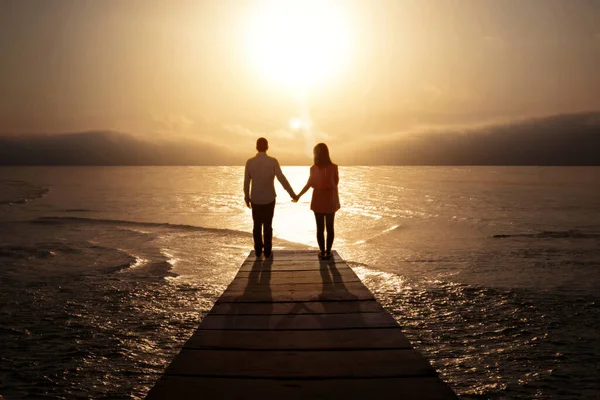 日落时分 年轻夫妇手牵手站在防波堤上的轮廓 — 图库照片