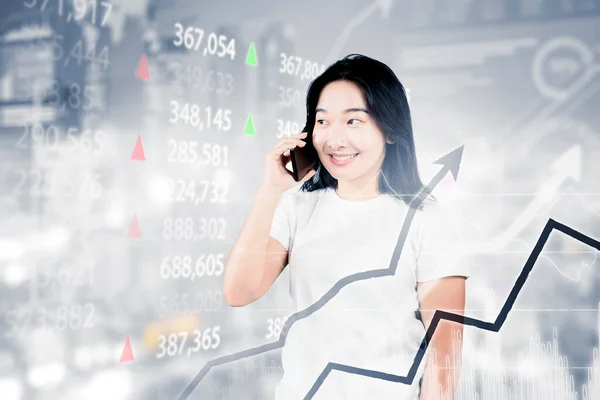 株式市場のグラフを背景に立ちながら携帯電話で話している若い女性の写真 — ストック写真