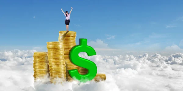 青い空を背景にお金のヒープ上に立ちながら手を上げることで成功を表現する幸せな実業家 — ストック写真