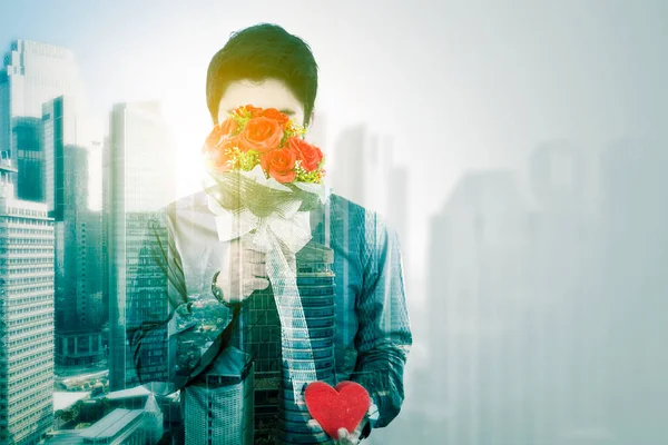 赤いバラの花で顔を隠しているビジネスマンの二重の露出は 彼のガールフレンドに驚きを与えながら 背景の街並みに立って — ストック写真