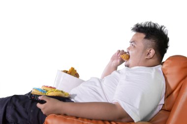 Obezite uzmanı stüdyoda televizyon izlerken koltukta kızarmış tavuk yiyor. Beyaz arkaplanda izole
