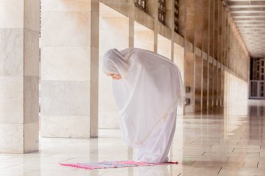 Camide Ruku jesti yaparken dua kıyafeti giyen genç bir kadın.