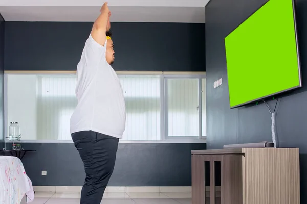 肥胖男子穿着运动服在家里带着绿屏的电视机前锻炼的侧视图 — 图库照片
