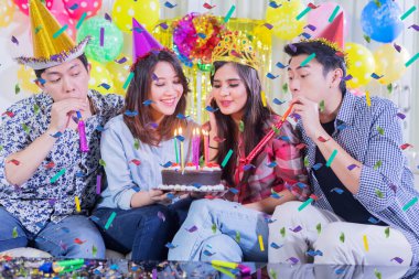 Bir grup mutlu insan doğum gününü evde kutlarken pastaya mum üflüyorlar.