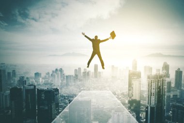 Ofisin çatısından atlarken elinde bavul taşıyan işadamının arka görüntüsü.