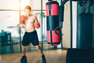 Erkek boksör spor salonunda dururken kum torbasıyla egzersiz yapıyor.