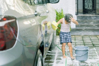 Sevimli küçük çocuk evde araba yıkarken babası tarafından su püskürtülmüş.