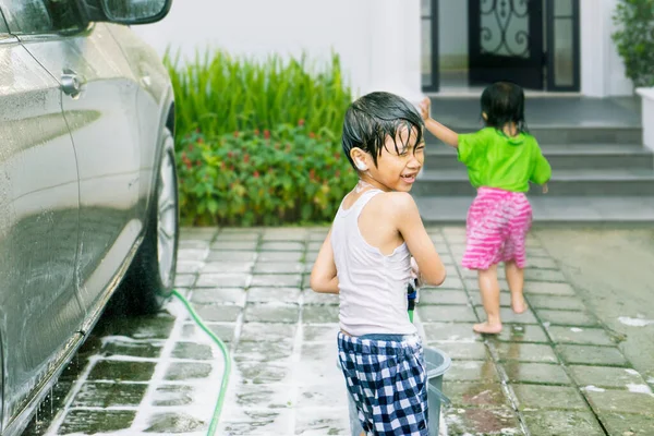 家で車を洗いながら水遊びをしている2人の幸せな子供 — ストック写真