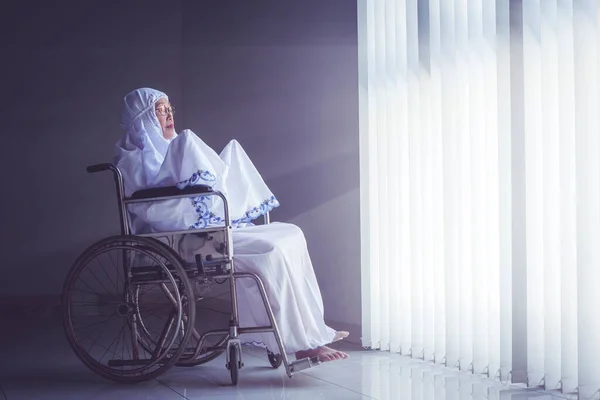 Старшая Женщина Молится Аллаху Сидя Инвалидной Коляске Возле Яркого Окна — стоковое фото