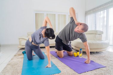 Spor kıyafetleri giyen genç bir çift evdeki oturma odasında birlikte spor yapıyorlar.