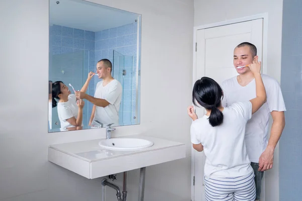 一对年轻夫妇站在浴室的镜子前互相刷牙 在家里中弹 — 图库照片