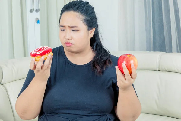 Товста Жінка Виглядає Сумнівно Тримаючи Яблуко Пончики Вітальні Постріл Вдома — стокове фото