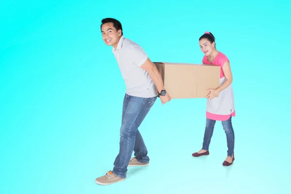 一对快乐的年轻夫妇带着纸板箱在工作室里搬入有托斯卡背景的新房子 — 图库照片