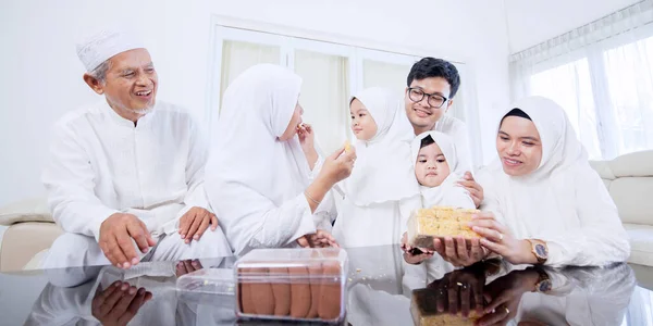 开开心心的三代穆斯林家庭在开斋节期间一起吃饼干 同时坐在客厅的沙发上 在家里中弹 — 图库照片
