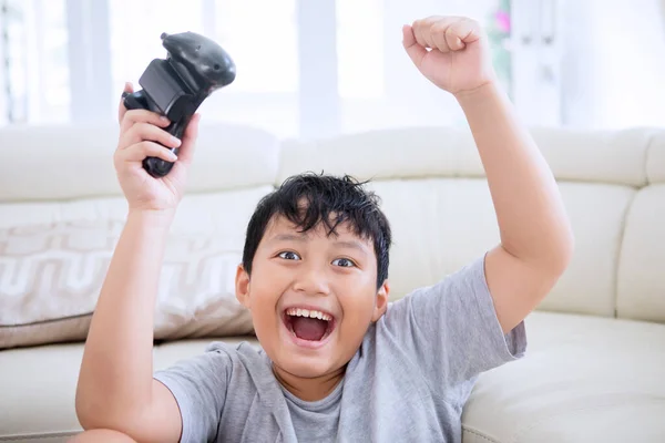 소년은 거실에서 비디오 게임을 하면서 승리를 축하하기 조이스틱을 올린다 가정에서 — 스톡 사진