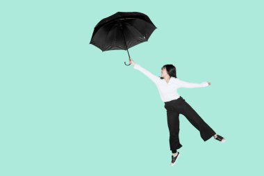 Young businesswoman holding an umbrella while jumping in the studio with tosca background