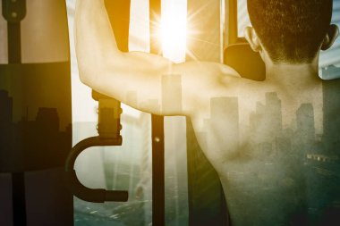 Kentin arka planında dururken ağırlık kaldırma makinesiyle egzersiz yapan kaslı adamın çifte pozu