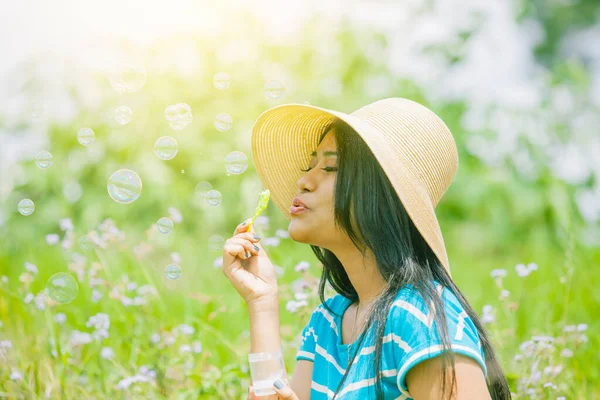 太陽の光を背景に花畑でシャボン玉を吹いている間に帽子をかぶっている若い女性のクローズアップ — ストック写真