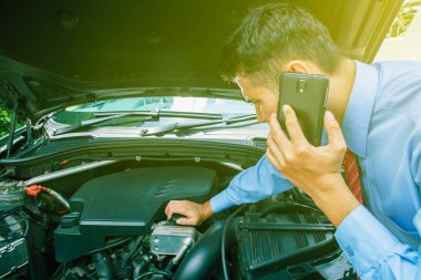Genç işadamı yardım için telefon açarken bozuk araba makinesini kontrol ediyor.