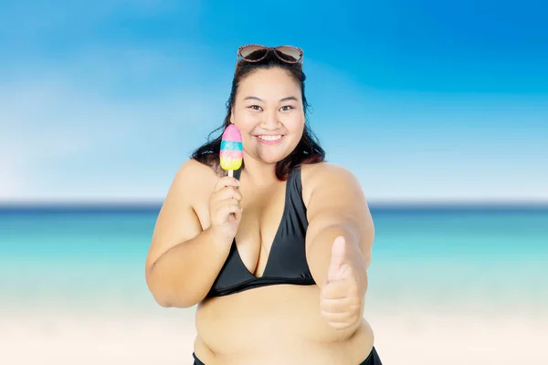胖女人拿着冰激凌站在沙滩上 蓝天巴赫站在镜头前 伸出大拇指 — 图库照片