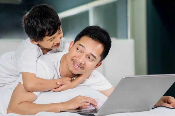 Menino Abraçando Seu Pai Enquanto Usa Laptop Cama Tiro Casa — Fotografia de Stock