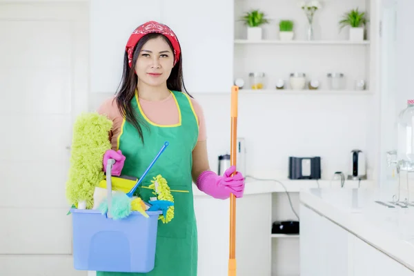 Όμορφη Νεαρή Γυναίκα Κρατώντας Εργαλεία Καθαρισμού Ενώ Στέκεται Στην Κουζίνα — Φωτογραφία Αρχείου