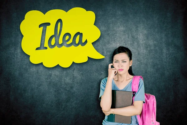 Female student thinking with eyes closed while standing with idea word on the cloud speech bubble in classroom