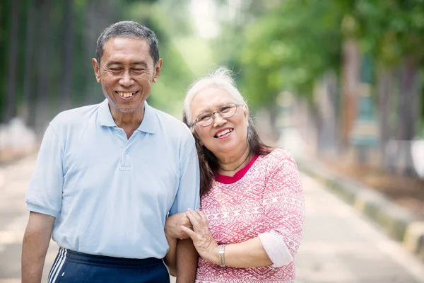 Happy old couple smiling at the camera while standing at the park