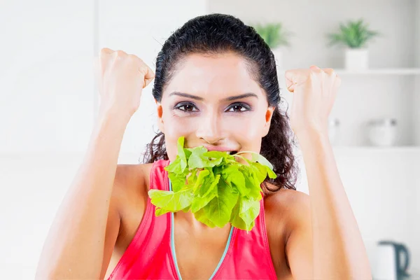 Young woman expressing happy while biting leaves of raw spinach in her mouth. Shot at home