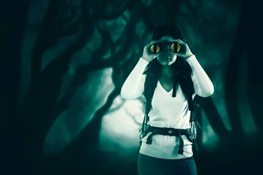 Dürbün kullanan kadın yürüyüşçü sisli arka planla ormanda dikilirken