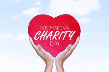 Close up of unknown hands holding a heart symbol with world charity day text in the blue sky background