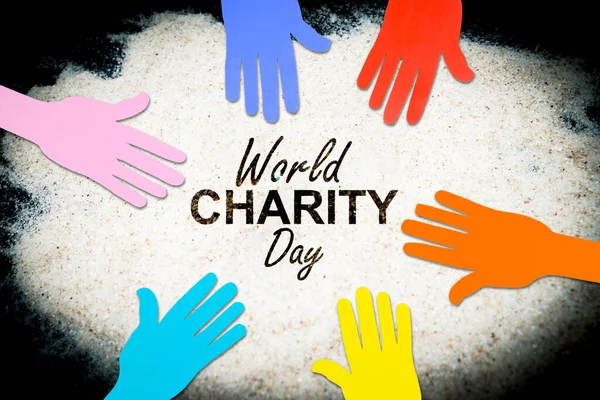 Top down view of colorful paper hands above the sand with world charity day text