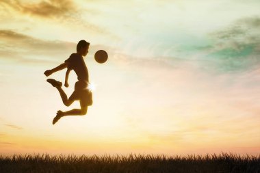 Futbol sahasında maç yaparken top ile zıplayan erkek futbolcunun silueti.