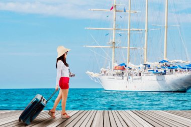 Yat geçmişli ahşap iskelede yürürken bavul taşıyan genç bir kadın.