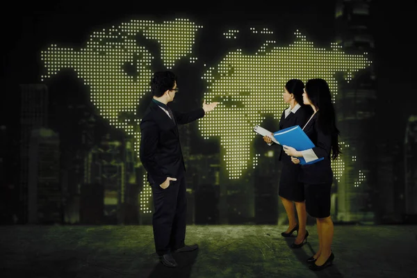 Three business people showing world map in the virtual screen while discussing and meeting in the office with