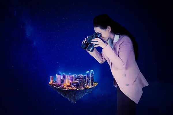 女商人用双筒望远镜站在夜空中凝视着发光的城市 — 图库照片
