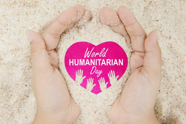 Top down view of unknown hands holding sand with world humanitarian day text on the heart symbol