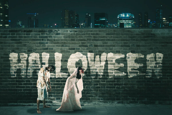 Two spooky ghost walking with halloween word on the brick wall at night time