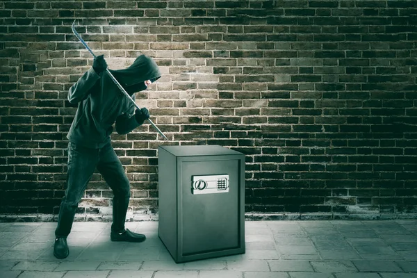 男子抢劫犯站在砖墙背景下 用撬棍砸破保险库 — 图库照片