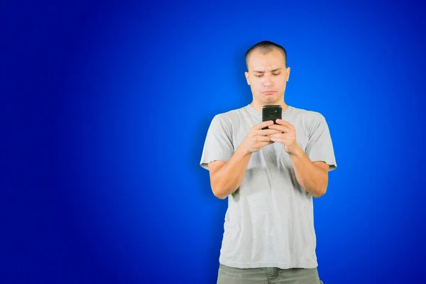 白人男人用手机表达困惑 站在有蓝色背景的工作室里 — 图库照片