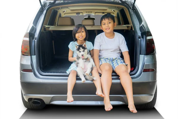 两个快乐的小孩和他们的狗坐在汽车行李箱里 因白人背景而被隔离 — 图库照片