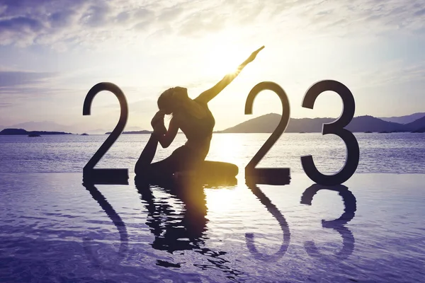有2023个号码的年轻女子在沙滩上练习瑜伽的轮廓 背景为黎明阳光 — 图库照片