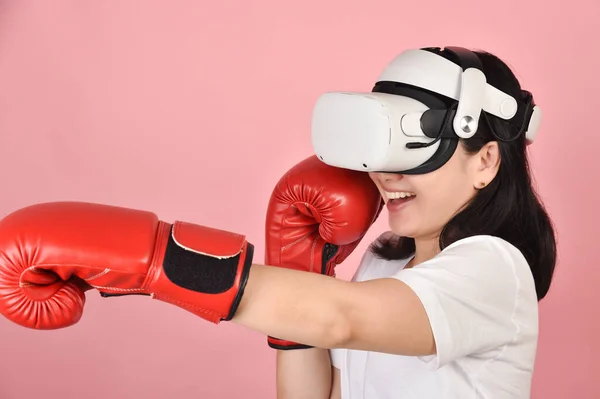 Asian woman hitting a punch by vr glasses, Working out with boxing video games application from virtual reality headset, Young woman enjoy new fitness experience by vr technology, Studio shot.
