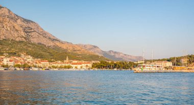 Günbatımında Hırvatistan 'ın Makarska kentinin panorama manzarası. Arka planda küçük tekneler ve Biokovo dağları var. Yaz havası, yumuşak sıcak renkler.