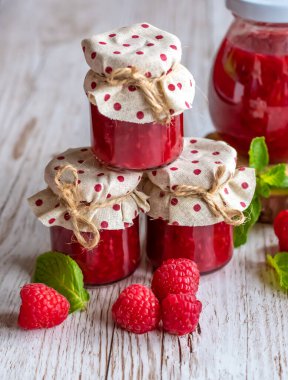 Raspberry marmalade in small glasses is placed on wooden desk. Homemade jam from fresh raspberries. Fresh and healthy cooking.