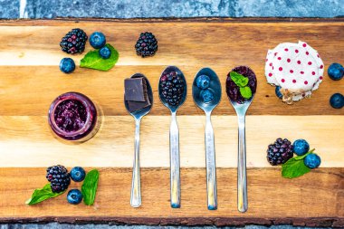 Blueberry, blackberry and chocolate are placed in silver spoon on wooden desk. Ingredients for marmalade. Fresh fruit around.