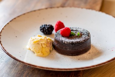 Çikolata şekerleme (cupcake), ahududu, dondurma kreması ve tabağa konmuş pudra şekeri ile