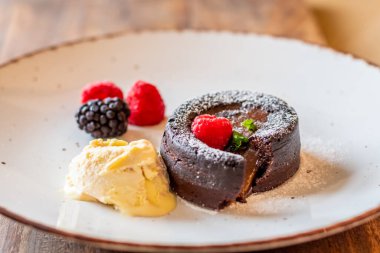 Çikolata şekerleme (cupcake), ahududu, dondurma kreması ve tabağa konmuş pudra şekeri ile