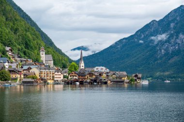 Hallstatt Village ve Hallstatter. Avusturya 'da göl. Göl kenarındaki ünlü eski kilisenin manzarası. Arka plandaki dağların üzerinden bulutlar ve sis. Ünlü turizm beldesi.