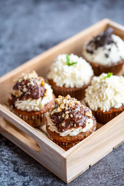 Cupcakes and muffins placed in wooden box. Chocolate and creme with nuts. Fresh home make baked sweets.